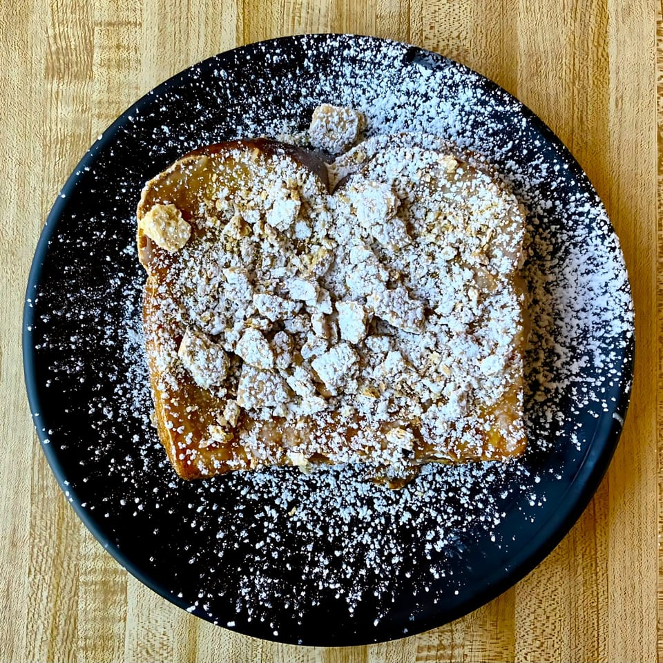 Brookies Cafe's French toast, topped with powdered sugar and crumble, on a black plate.