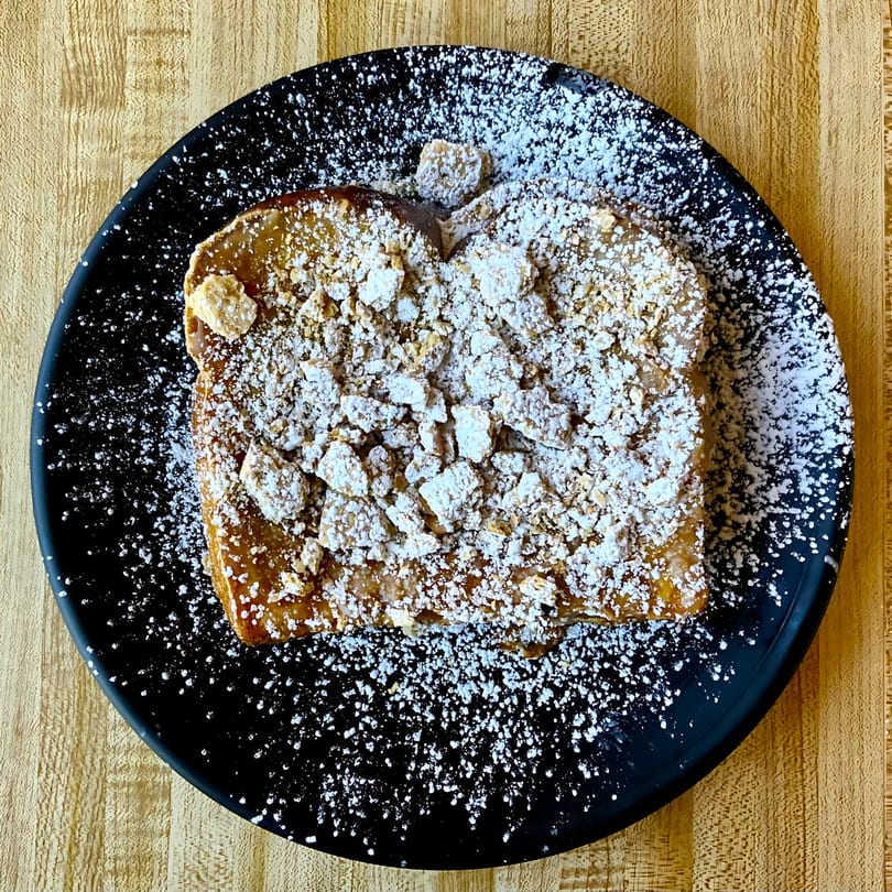 Brookies Cafe's French toast, topped with powdered sugar and crumble, on a black plate.