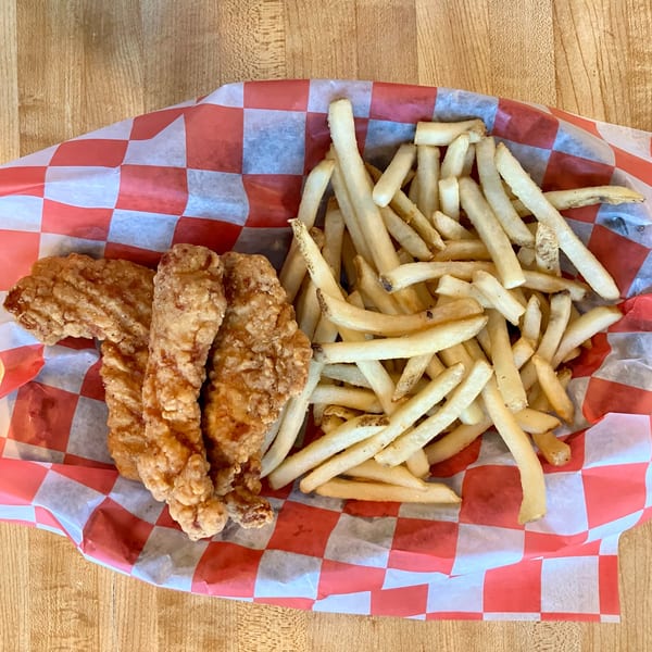 Three crispy fried chicken tenders and a pile of golden french fries in a red and white checkered basket.