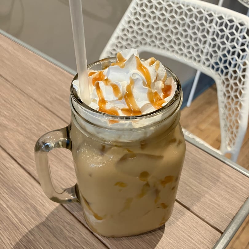 Iced coffee with whipped cream and caramel drizzle in a mason jar on a wooden table.