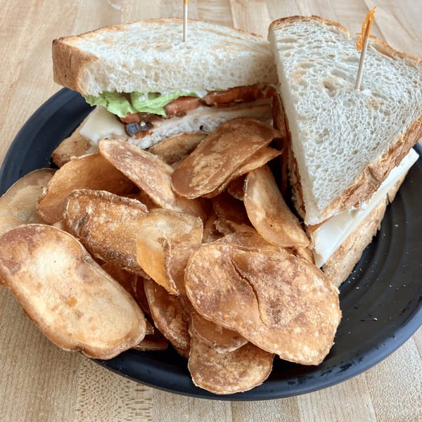 A toasted sandwich with lettuce, tomato, and cheese, served with a side of potato chips.