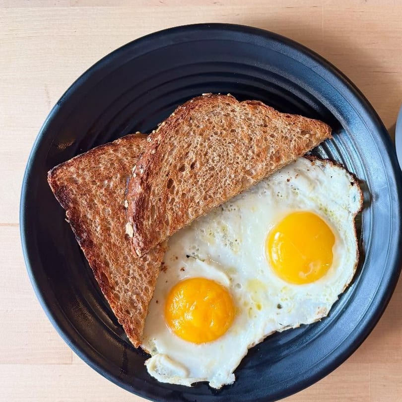 Two fried eggs with bright yellow yolks and two slices of toasted bread on a black plate.