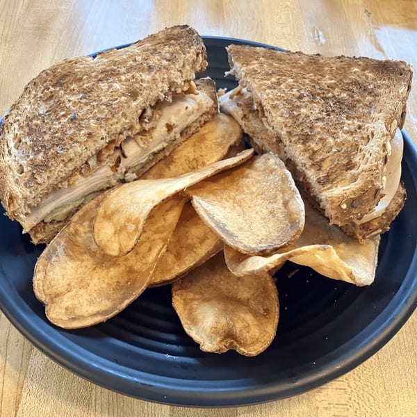 Toasted turkey sandwich with avocado and chips on a black plate at Brookies Cafe.