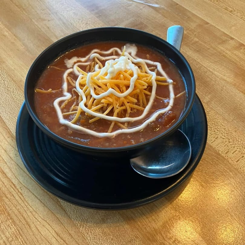 A black bowl of Brookies Cafe chili, topped with shredded cheese and a swirl of sour cream.
