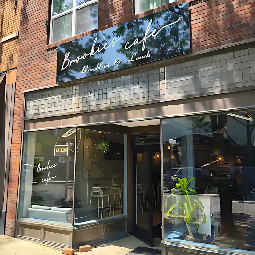 The exterior of Brookies Cafe, a brick building with large glass windows and an "OPEN" sign.