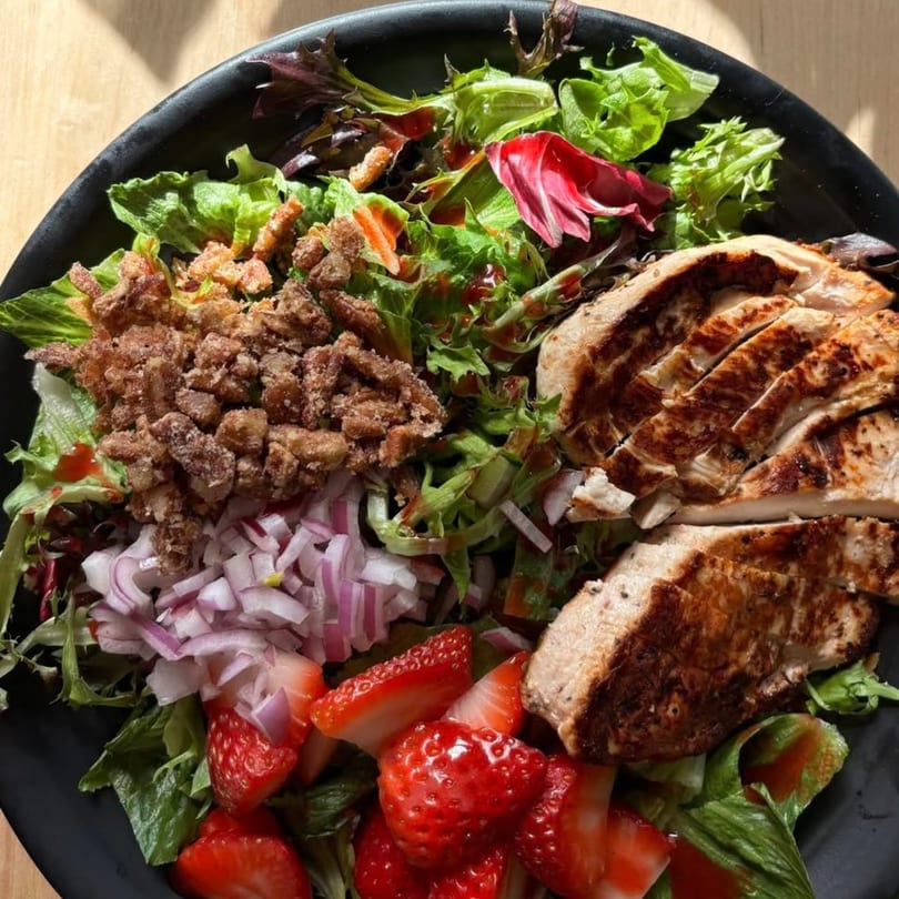 A vibrant salad with grilled chicken, strawberries, red onions, candied pecans, and mixed greens.